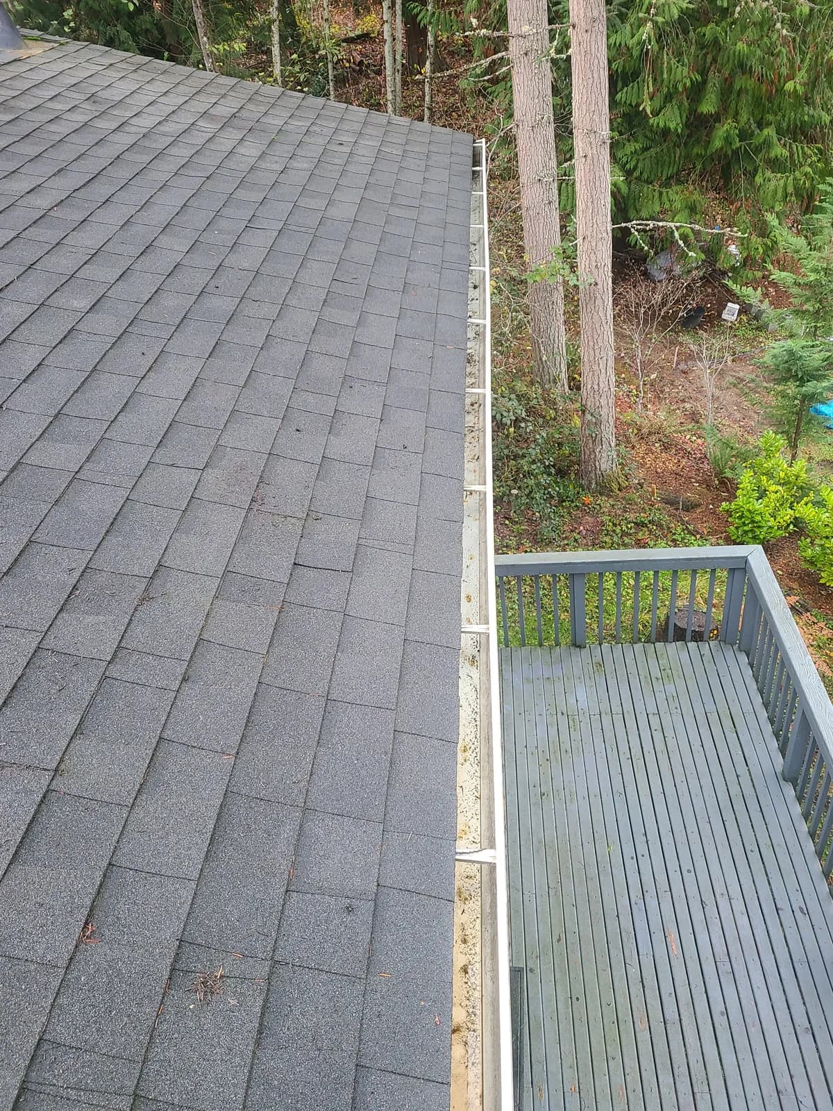 After — Gutter packed solid with pine needles beside a wood deck, restored to a clean empty channel