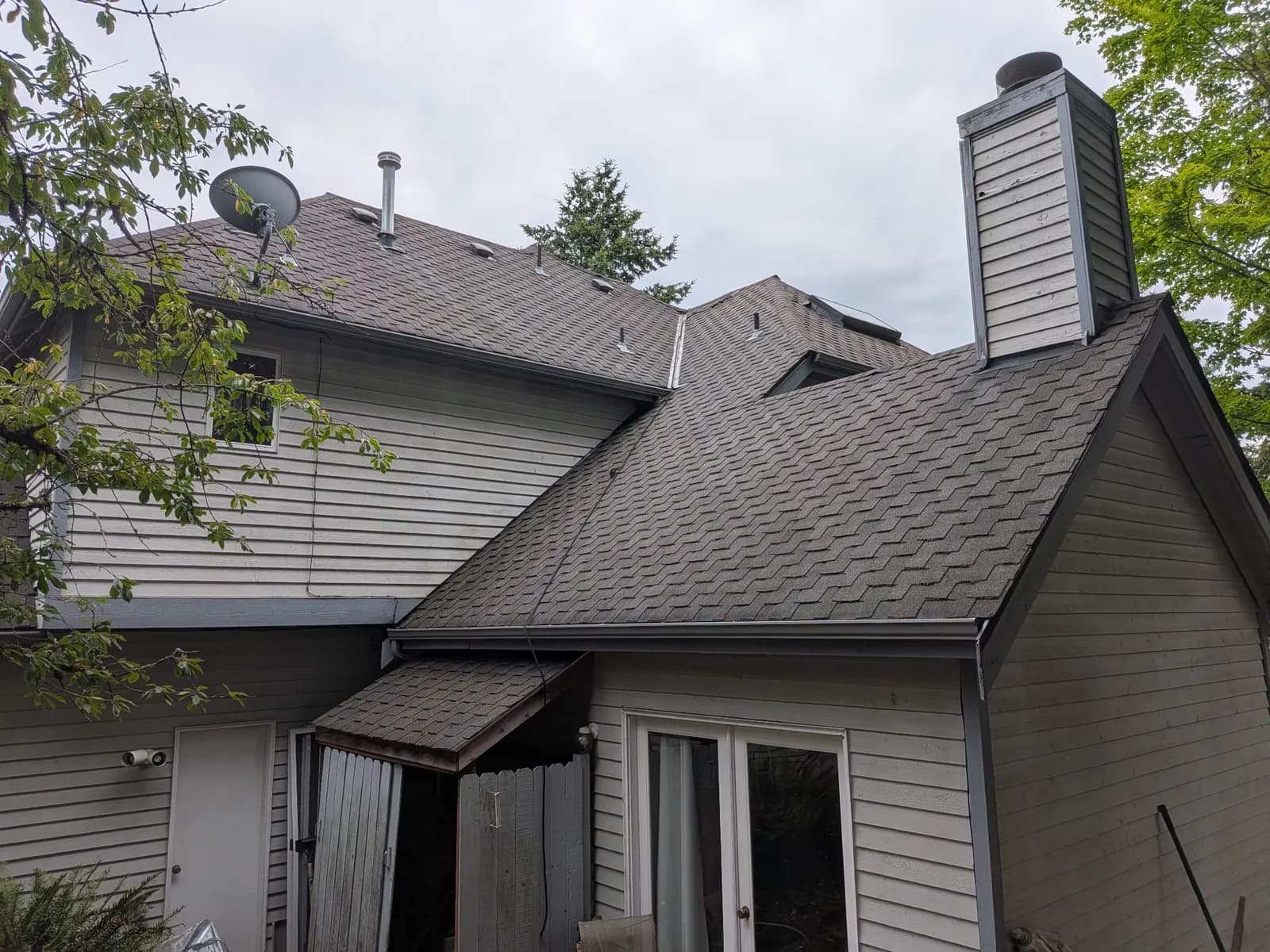 After — Two-story home with moss-covered shingles on every roof face, spotless after moss removal