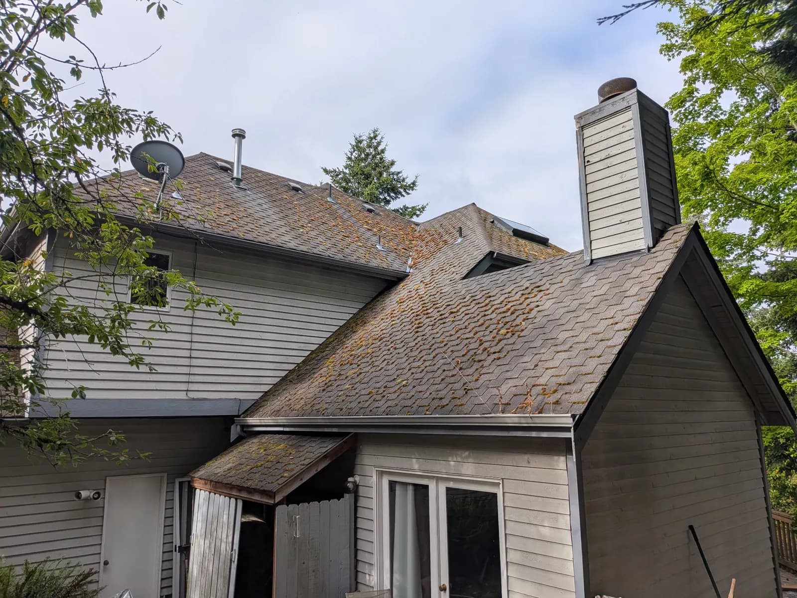 Before — Two-story home with moss-covered shingles on every roof face, spotless after moss removal