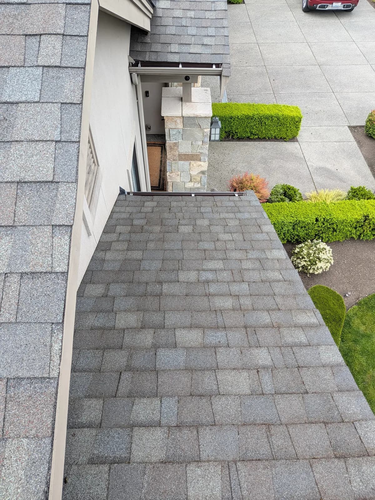 After — Moss-filled shingle grooves beside a stone chimney, cleared to a spotless roof plane